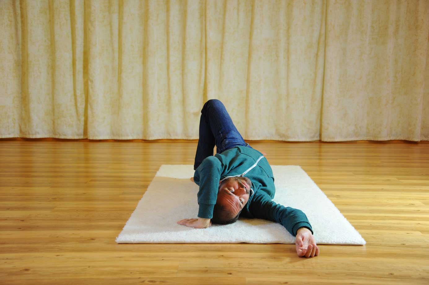 Mann übt zuhause via Zoom im Feldenkrais Kurs auf einer weichen Matte am Boden